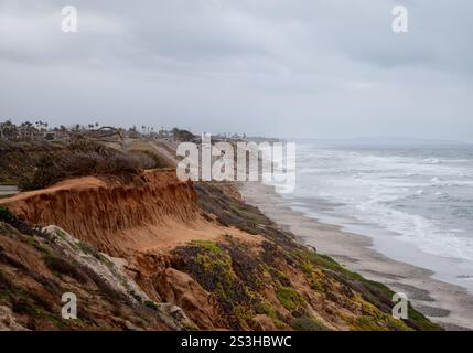 Waves crash against the sandy beach in Carlsbad, California while coastal erosion exposes vibrant earth tones. Pacific Coastal HIghway runs parallel t Stock Photo