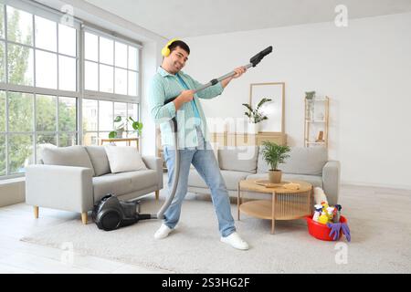 Young man having fun while vacuuming carpet and listening to music in room Stock Photo