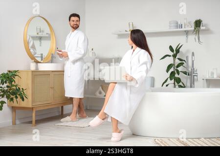 Handsome man brushing teeth while his wife using laptop in bathroom Stock Photo