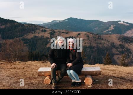 A couple is sitting on a tree log. Behind the couple is the Carpathian mountain range. Autumn view. Picture that reflects harmony and peace. Stock Photo