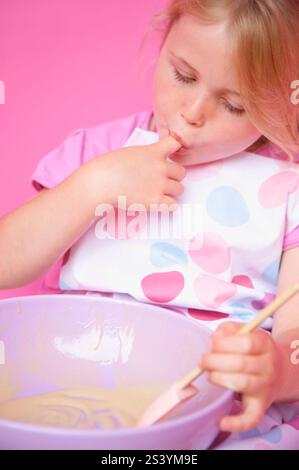 Young girl holding a baking bowl sucking her finger Stock Photo