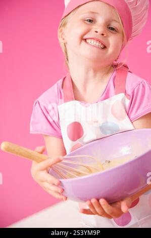 Smiling young girl holding a baking bowl and a whisk Stock Photo