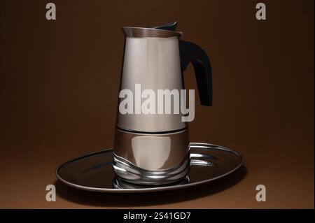 A chrome-plated coffee pot sits on a plate on a brown background Stock Photo