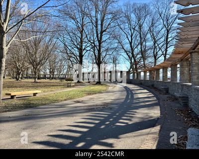 Curved pathway with benches and a stone pergola in a tree-lined park Stock Photo