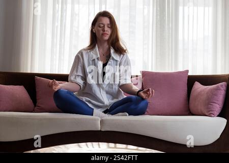 Young woman meditating on couch at home Stock Photo