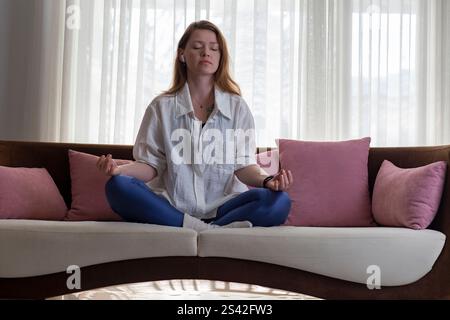 Young woman meditating on couch at home Stock Photo