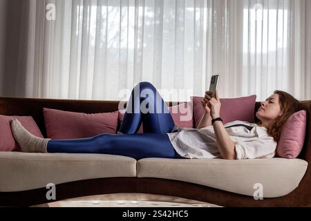 Young woman lying on a couch and looking at her smartphone Stock Photo