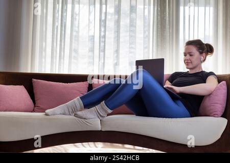 Young woman using laptop and wireless headphones at home Stock Photo
