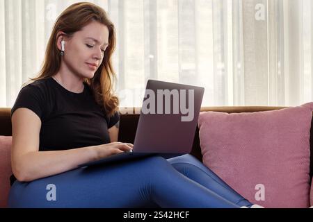 Young woman using laptop and wireless headphones at home Stock Photo