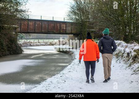 Couple walking along the snow covered towpath of the frozen Trent and Mersey canal near Wheelock Cheshire Stock Photo