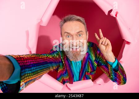 Eccentric senior man in colorful outfit posing against torn pink background Stock Photo