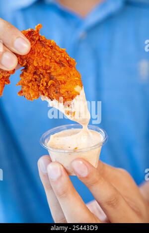Man holding fried chicken strip dunking in spicy mayo sauce. Stock Photo