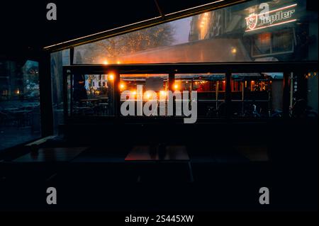 Cozy evening view through a café window with warm lights reflecting on glass. A mix of indoor and outdoor ambiance with bicycles and a charming urban Stock Photo