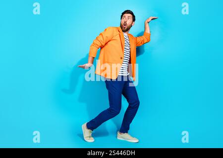 Charismatic young man in vibrant orange jacket striking a playful pose against a vibrant teal background Stock Photo