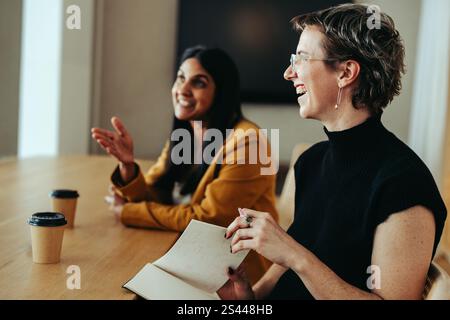 A casual meeting between colleagues in an office setting, featuring two women engaged in conversation. They appear relaxed and friendly as they share Stock Photo