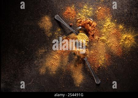 Spoons with various spices and spices scattered around on a black table. Flat lay Stock Photo