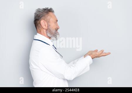 Mature doctor in white uniform presenting with open hands against neutral background Stock Photo