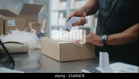 African American Warehouse Clerk Packs Cardboard Box with Online Order, Scans Code, Uses Tablet Computer, Prepares Parcels for Shipping. Sorting Center of E-Commerce Store, Delivery Service. Close Up Stock Photo