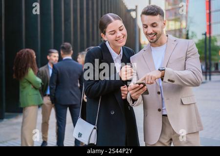 Colleagues Smiling and Sharing Ideas on a Smartphone Outdoors Stock Photo