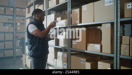 African American Inventory Specialist Walks in Warehouse Retail Facility, Scans Parcels with E-Commerce Online Orders, Checks Delivery Information on Tablet Computer. Sorting Center of Postal Service. Stock Photo