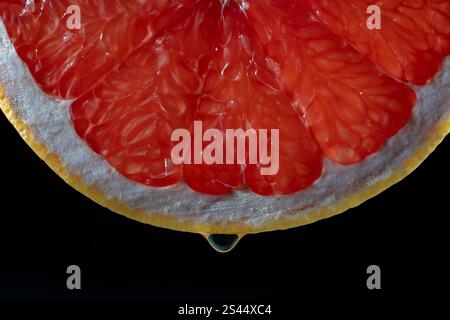 Juicy red grapefruit slice with drop on black background . Texture fresh citrus fruit, close up, healthy sweet food. Macro photography Stock Photo
