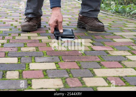 Man picking up lost black leather wallet full of money banknotes on city street, copy space, close up. Concept of lost or found wallet with cash money Stock Photo