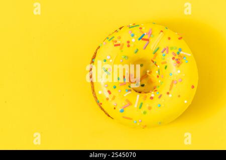 Donut on yellow background with colorful sprinkles. Top view Stock Photo