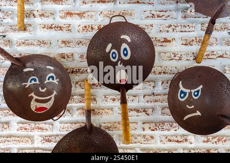 Old frying pans with painted faces, hang on a brick wall, close up Stock Photo
