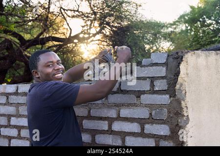 bricklayer african men, using metal masonry reinforcement to reinforce bricks, building a wall at sunset outdoors Stock Photo