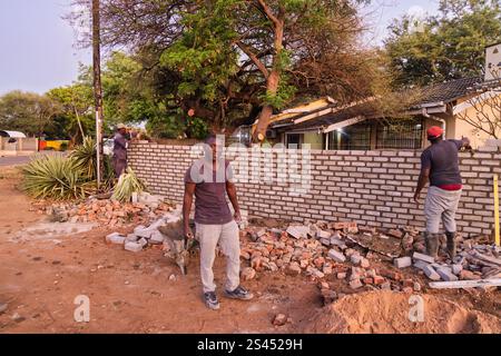 bricklayer african men colleagues , pushing wheelbarrow, using a trowel and align string, building a wall at sunset outdoors, rubble around Stock Photo