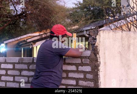 bricklayer african men alone, using a trowel and yellow bubble spirit level, building a wall at sunset outdoors Stock Photo