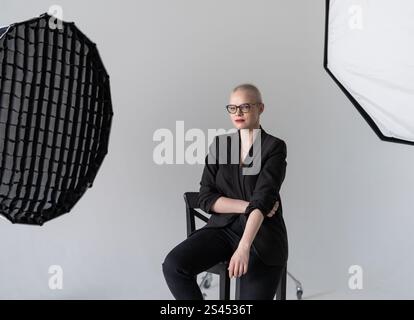 A professional woman poses confidently while seated in a photography studio with softbox lighting equipment, wearing formal business attire. Smiling W Stock Photo