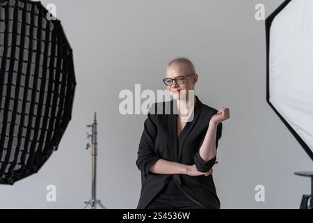A professional woman poses confidently while seated in a photography studio with softbox lighting equipment, wearing formal business attire. Smiling W Stock Photo