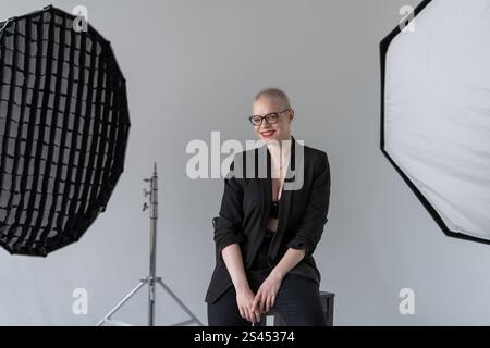 A professional woman poses confidently while seated in a photography studio with softbox lighting equipment, wearing formal business attire. Smiling W Stock Photo