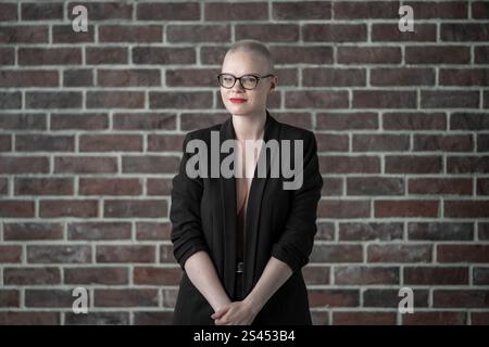 A professional woman poses confidently while seated in a photography studio with softbox lighting equipment, wearing formal business attire. Smiling W Stock Photo