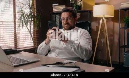 Caucasian business male relaxing entrepreneur leader using mobile phone in office guy businessman boss agent ceo typing smartphone cyberspace addict Stock Photo