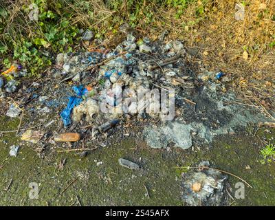 Pile of burnt and unburnt trash rubbish with plastic debris and ash on the side of a road in a natural setting - fly tipping newcastle upon tyne uk Stock Photo