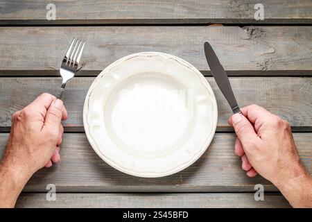 Hungry man waiting for his meal over empty plate on wooden table. Stock Photo