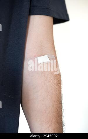 Small plaster and patch on an unrecognizable man's arm after blood test or donation. Close up shot, white background Stock Photo