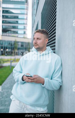 Successful young Caucasian man walking outside office building, engineer software developer programmer smiling and happy using test app on phone  Stock Photo