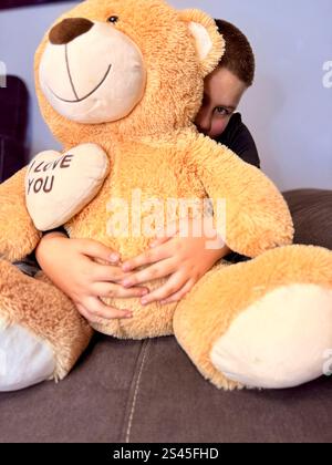 Full length portrait of a happy little boy holding teddy bear and showing thumbs up gesture isolated over blue background. High quality photo Stock Photo