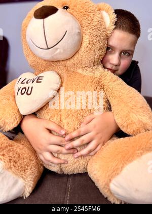 Full length portrait of a happy little boy holding teddy bear and showing thumbs up gesture isolated over blue background. High quality photo Stock Photo