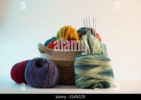 A variety of colorful yarns neatly arranged in a basket, accompanied by knitting needles, set against a clean white background, showcasing creativity Stock Photo