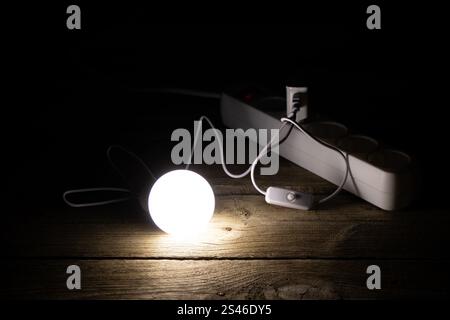 An energy-saving light bulb is on the wooden floor near the socket, the light of the lamp Stock Photo