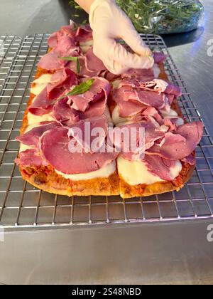 Fresh baked focaccia or pala romana Rectangular pizza with smoked meat ham and pastrami on wire rack for sale Stock Photo