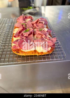 Fresh baked focaccia or pala romana Rectangular pizza with smoked meat ham and pastrami on wire rack for sale Stock Photo