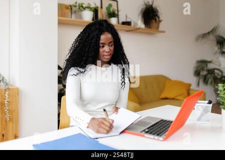 Focused young black woman taking notes while working remotely from home office Stock Photo