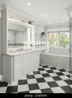 Vanity and platform tub in bathroom with black and white checkerboard floor and marble floor and wall tile Stock Photo