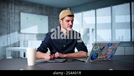 Happy Young Male Designer Using Laptop In Office Stock Photo
