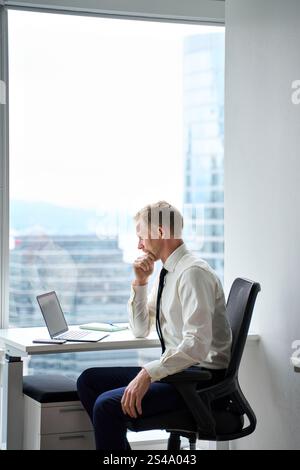 Busy young business man looking at laptop thinking working in office. Vertical Stock Photo
